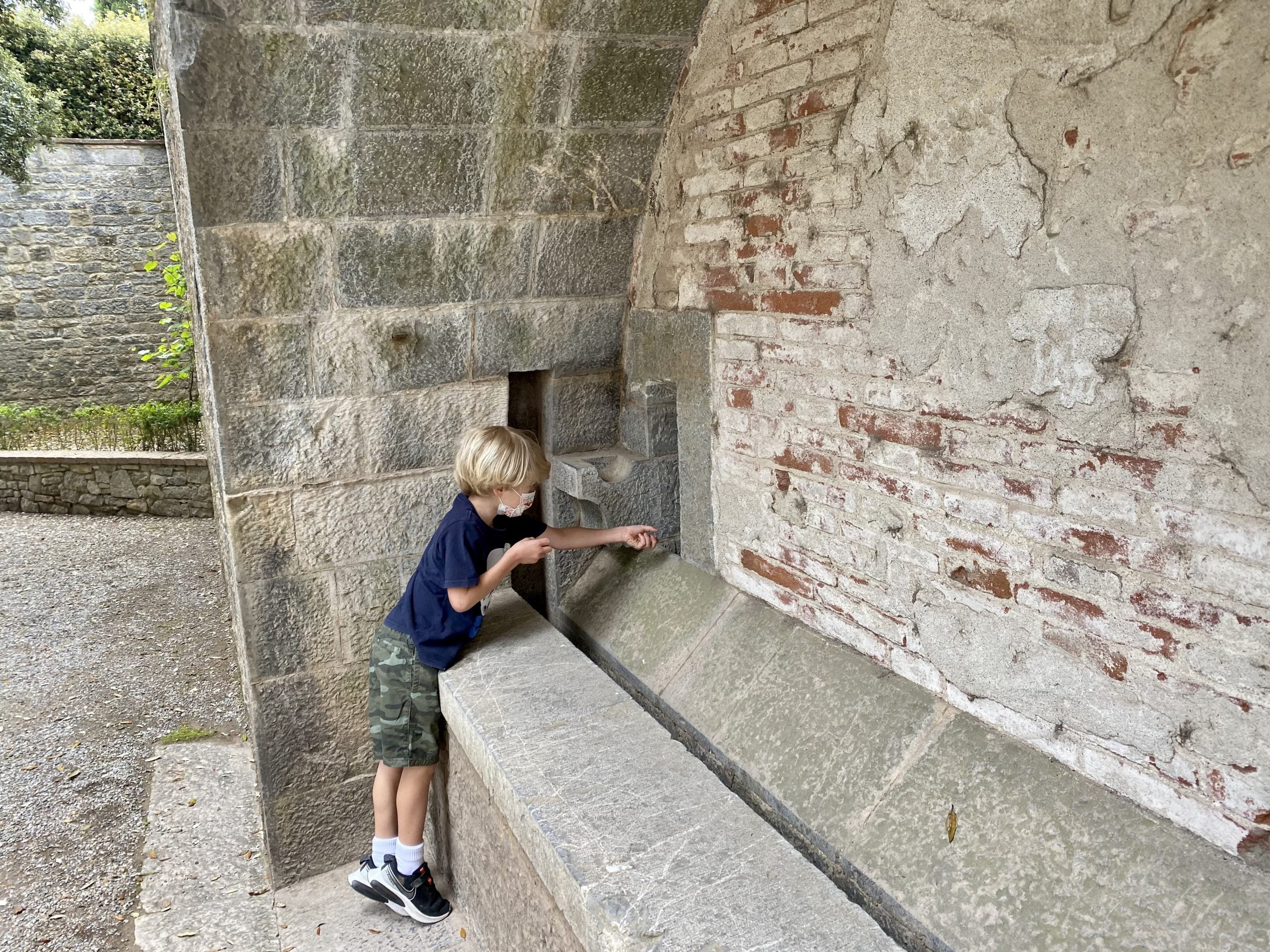 Little boy pretending to shoot at arrow through a narrow slit in a wall at Castello di Brolio (Brolio Castle).